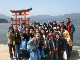 A group of students from a High School Exchange Program pose for a photo in front of the floating torii gate at Itsukushima Shrine in Miyajima, Japan.